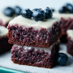 Decadent glazed blueberry brownies topped with a sweet glaze and fresh blueberries.